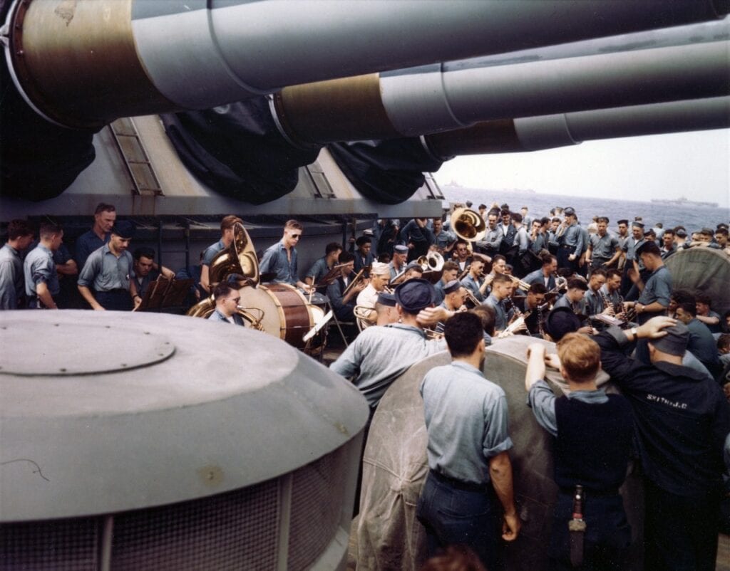 USS Wisconsin (BB-64) Band concert under the battleship's after 16/50 guns, while she was operating at sea with the Pacific Fleet, circa 1945. An aircraft carrier is faintly visible in the right distance. Sailor in right foreground has name J.C. Smith stencilled on his working jacket. Official U.S. Navy Photograph, now in the collections of the National Archives.